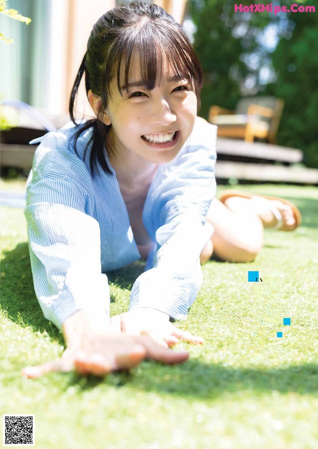 A young woman laying on the grass in a blue shirt.