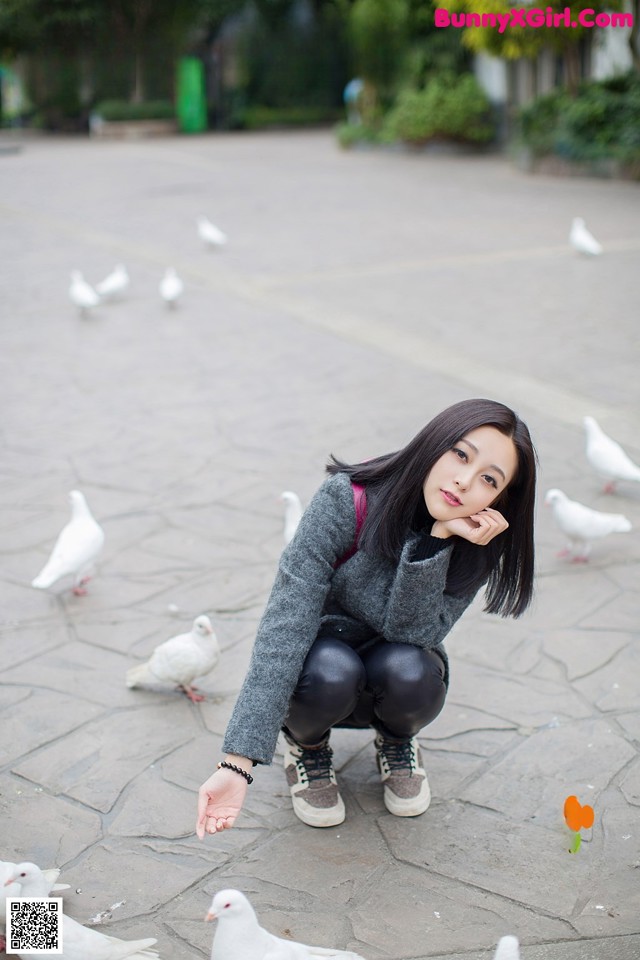 A woman crouching down in front of a group of white doves.