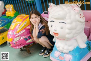 A woman in a school uniform standing next to a carousel.