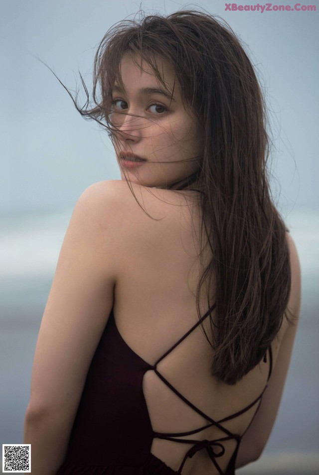 A woman in a black dress standing on a beach.