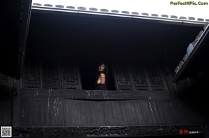 A naked woman sitting on a chair in front of a window.