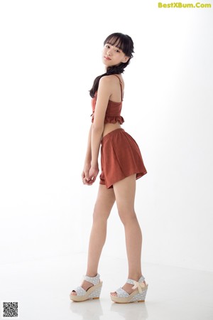 A woman leaning against a white wall wearing a brown top and shorts.