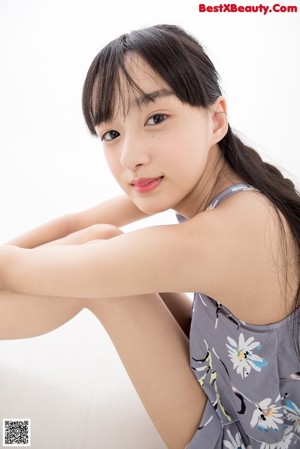 A woman standing in front of a white background wearing a gray floral romper.