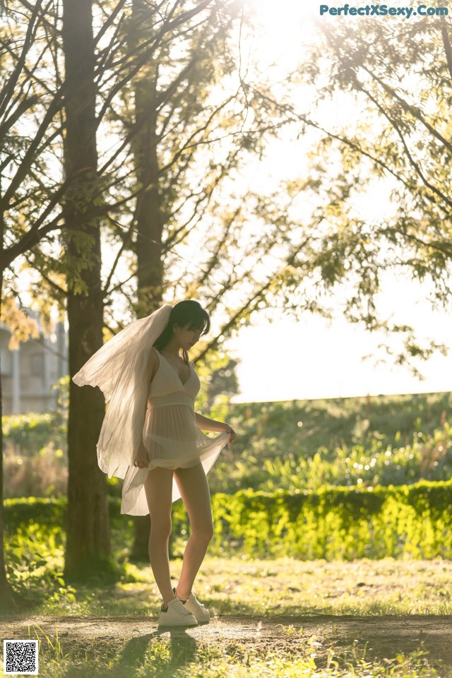 A woman in a white dress standing in a park.