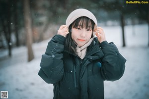 A woman standing in the snow wearing a black coat.