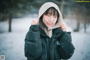 A woman standing in the snow wearing a black coat.