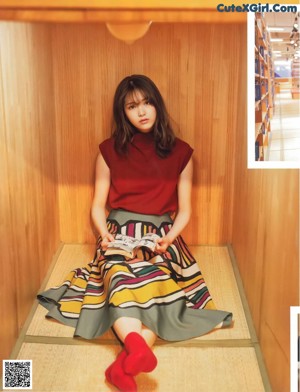 A woman in a blue top and black skirt sitting on a couch.