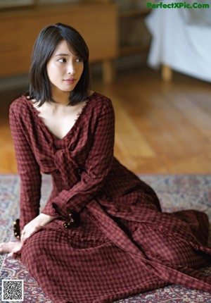 A woman sitting on top of a bed next to a window.