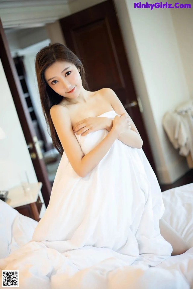 A woman in a white dress sitting on a bed.