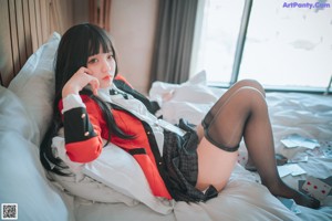 A woman in a red shirt and black stockings sitting on a bed.