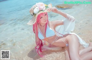 A woman in a white bikini sitting on the beach.