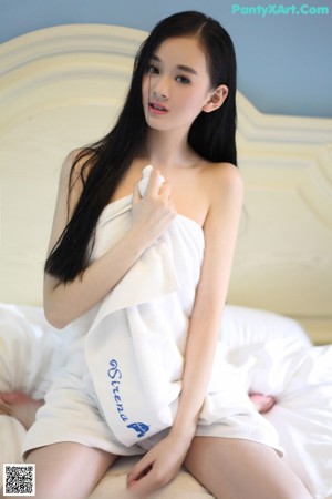 A woman in a white robe sitting on a bed.