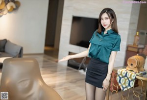 A woman in a green shirt and black skirt holding a red purse.