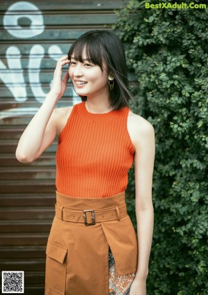 A woman in a brown top and patterned skirt standing on a sidewalk.