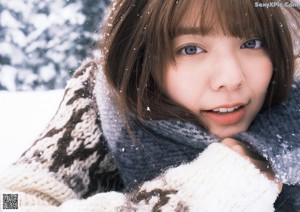 A woman standing in the snow in front of a tree.