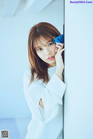 A woman leaning against a wall with her hand on her chin.