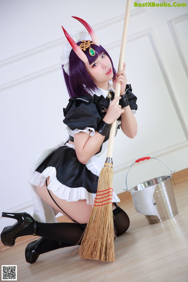 A woman dressed as a maid holding a broom.