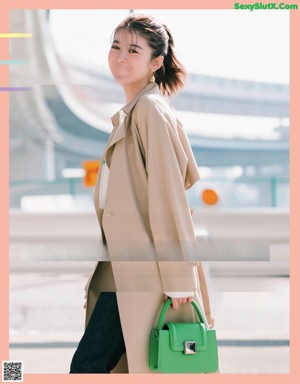 A woman in a white shirt and beige pants is holding a handbag.