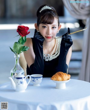 A woman sitting at a table with a cup of coffee and a rose.