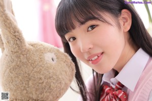 A young woman sitting on a bed with a teddy bear.