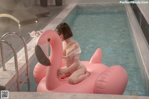 A woman in a white bodysuit sitting on an inflatable flamingo in a pool.